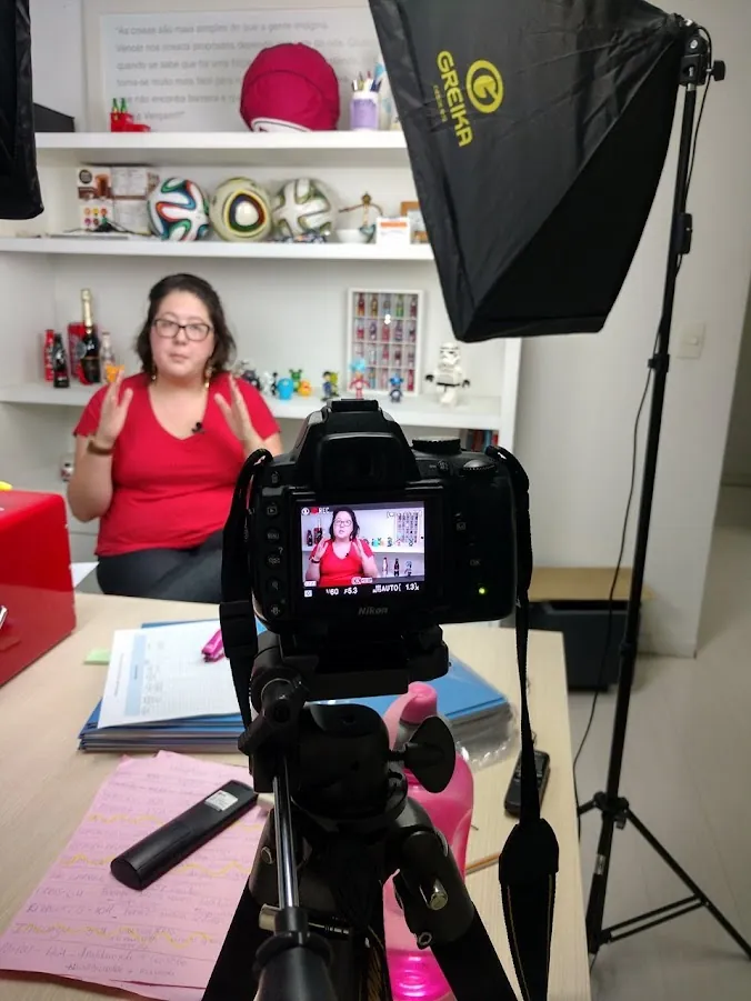 Clau Boaventura gravando aula no estúdio da BCOMB, vista por trás da câmera, com softbox e tripé