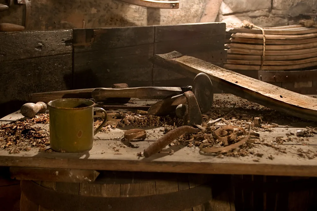 Bancada de uma velha oficina de carpintaria, com caneca, ferramentas e lascas de madeira.