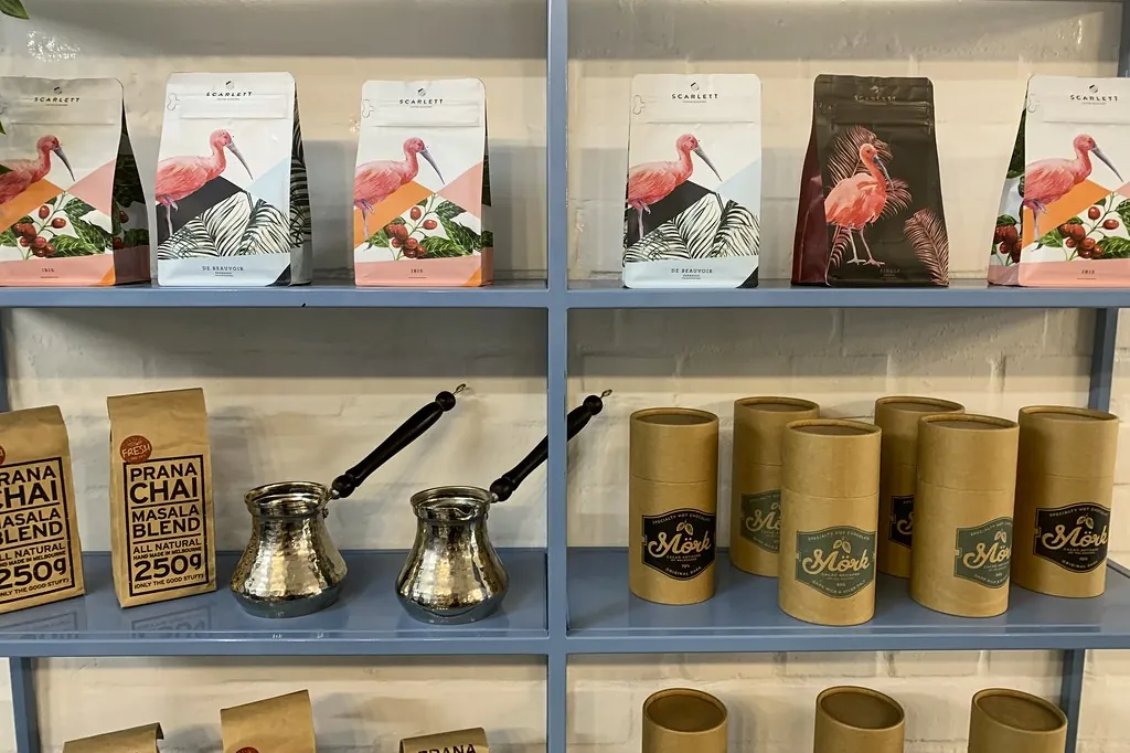 Prateleira de uma torrefação com pacotes de café ilustrados, latas de chá e bules de cobre.