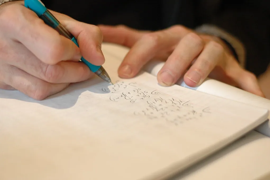 Mão escrevendo cálculos à mão num caderno, em close.